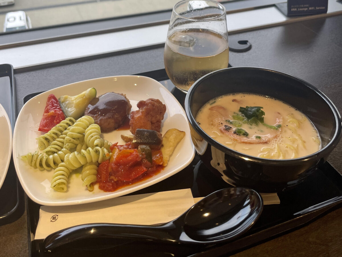 There are  ramen noodles with pork broth and foods from the buffet counter on the table.