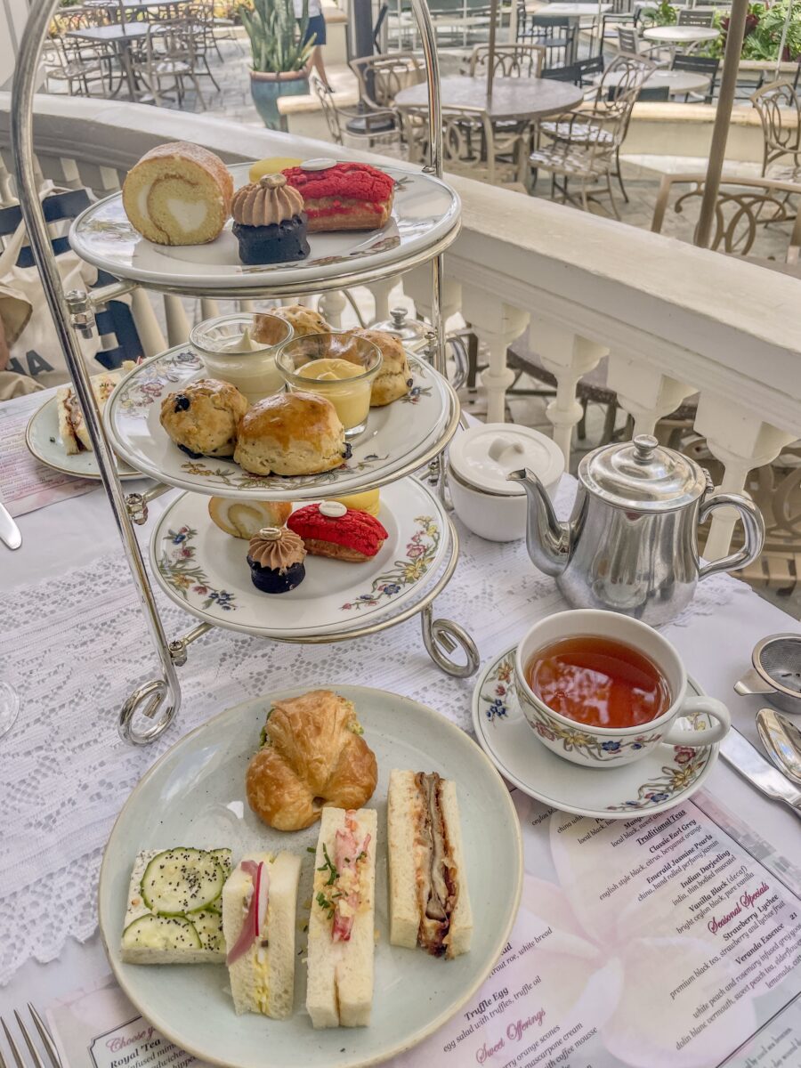 There is a three-tiered afternoon tea stand, sandwich plate, and tea on the table.